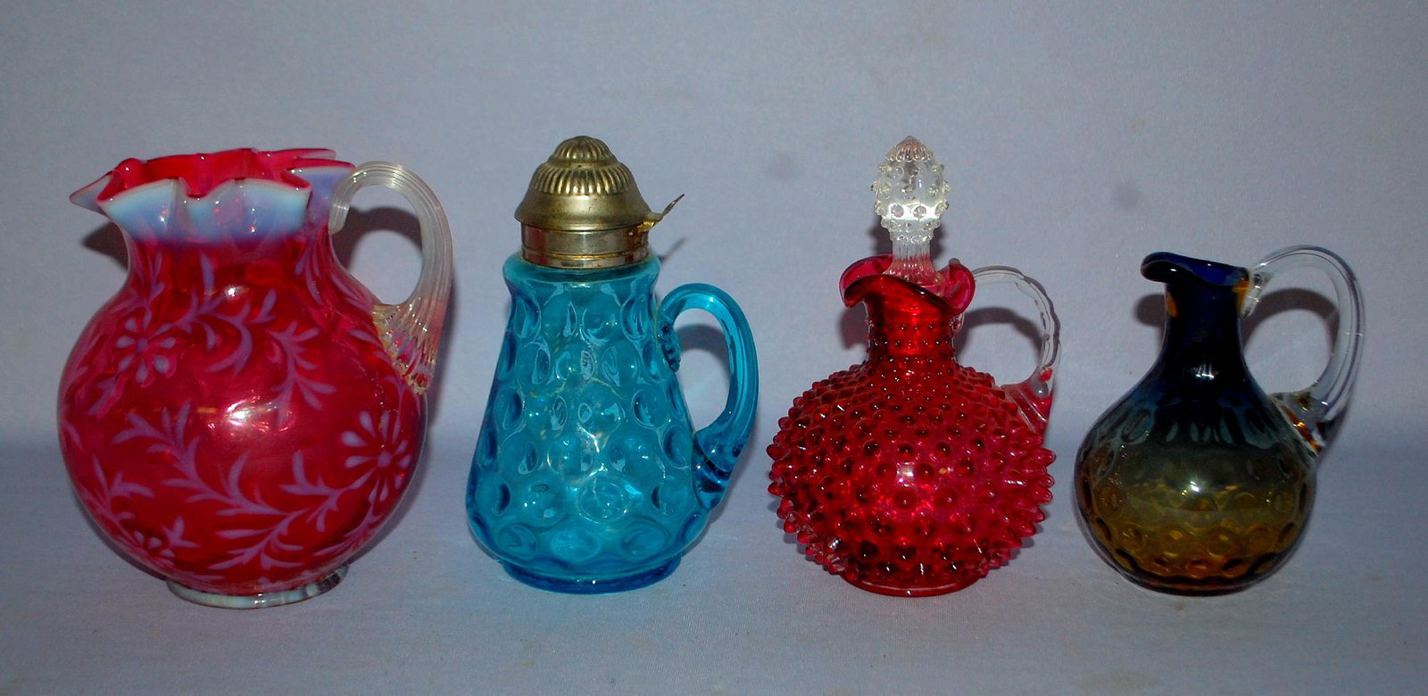 4 Victorian Colored Glass Collectibles. 1.) Cranberry: 4 Victorian Colored Glass Collectibles. 1.) Cranberry opalescent Daisy & Fern Pitcher. 2.) Blue thumbprint syrup with tin lid. 3.) Brown to blue thumbprint cruet, no stopper. 4.) Cranberry hobnail cru