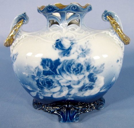 Flow Blue Vase w/Roses & Pierced Edges: Flow Blue Vase w/Roses: the rim has pierced designs. The handles have a gold wreath draped over them. Standing on 4 feet. Unmarked. (Worn gold trim.) 5 1/4" tall All items sell As Is, Where Is, no gua