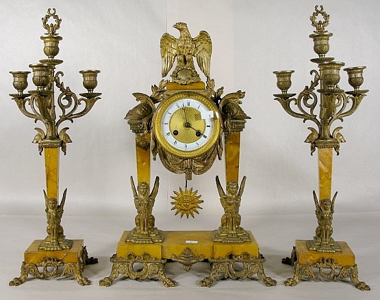 French Garniture, Bronze & Marble: French Garniture, Bronze & Marble: Roman style decoration of an eagle, helmets and winged figures on tan marble. With a 4" porcelain ring dial; dore center and bezel. (One candelabra has a damaged ste