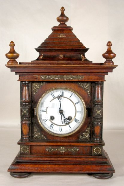 Oak Mantle Clock w/Brass Decor: Oak Mantle Clock w/Brass Décor: time and gong striking movement marked P.H. & S-19579. It has a 5 1/4" porcelain dial and a complete label inside the back door, in Swiss or German language. One name 