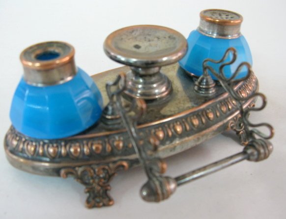 Blue Opaque Glass Ink & Pen Stand: Blue Opaque Glass Ink & Pen Stand: 2 blue opaque paneled bottles; 1 for the ink and 1 for sand; sitting in an oval metal frame with copper colored finish; decorative feet and border; pen holder for 3