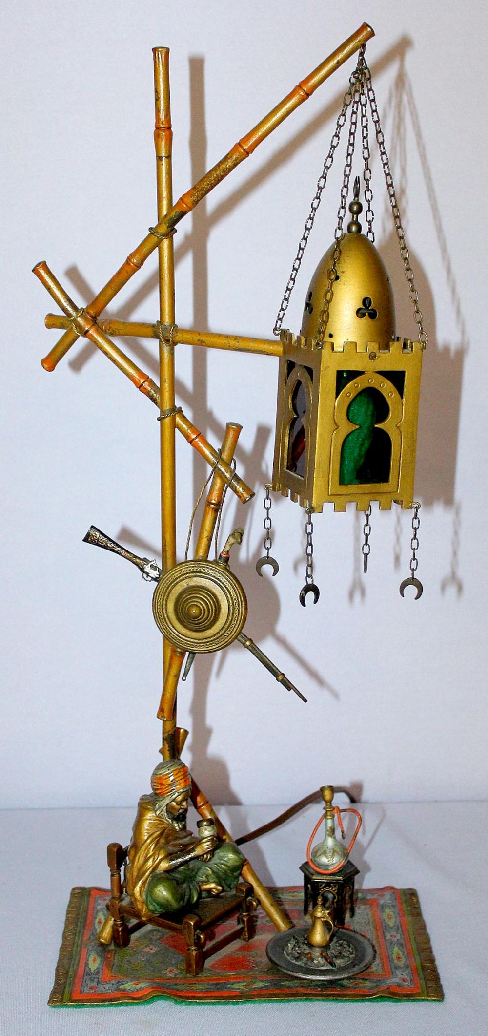 Antique Austrian Cold Painted Bronze Figural Lamp: Antique Austrian Cold Painted Bronze Figural Lamp w/ seated drinking tea on carpet w/ hookah, sheild, knife and sword hanging on lamp post, hanging light w/ red & green glass inserts. 19" T. **This Lo