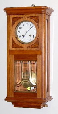German Spring Wound Hanging Clock: German Spring Wound Hanging Clock: time with strike on a single straight rod and lyre style pendulum. With a 6" porcelain dial. The mahogany case has beveled glass and carved designs. (The dial has a 