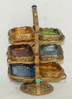 6 Pc. Salt Cellar Set in Jeweled Metal Stand: 6 Pc. Salt Cellar Set in Jeweled Metal Stand: the 6 salts are in 4 colors, with an acid cut. They and the metal stand have glass jewels around them, most likely from Czechoslovakia. Stand 6" T classic