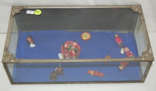 Display Case, Glass and Tin, Countertop: Display Case, Glass and Tin, Countertop: with floral designs on the corners of the lid; circa early 20th century; inside are several small plastic hollow dolls about 2" long. Case is 4 5/8" T x 14" W