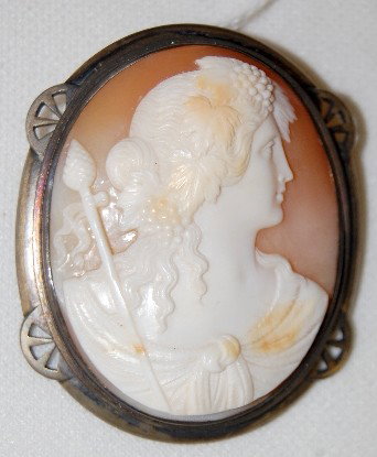 Carved Shell Classical Woman Cameo Brooch: Carved Shell Classical Woman Cameo Brooch: depicted is a figure of a woman with grape adorned hair in knotted gown and she is holding a scepter like object. In a heavy silver colored metal bezel, it i