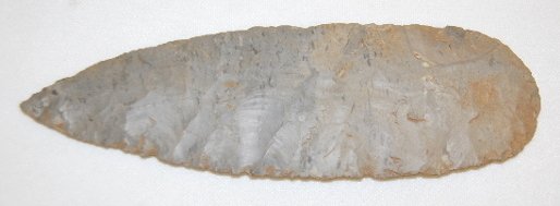 Chipped Blade w/Rounded End, 7 3/8": Chipped Blade w/Rounded End, 7 3/8": made from dark bluish gray material and has no notches; large, flat flakes were removed then the edges were formed with tiny crude nicks removed.