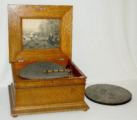 Oak Regina Disk Music Player: Oak Regina Disk Music Player: Has a nice interior picture of a man sitting on a bench as a religious group comes up the trail by him; comes with 8 disks; has the winding key. Working at this time. 12
