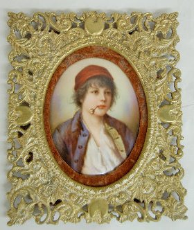 Hand Painted Porcelain Gypsy Boy In Gilt Frame: Hand Painted Porcelain Gypsy Boy in Gilt Frame: the unsigned porcelain oval shows a Gypsy boy wearing a red hat and a blue jacket with a pipe in his mouth; in an ornate heavy gilt frame with heart and
