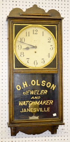 Waterbury "Pelican" Oak Advertising Wall Clock: Waterbury "Pelican" Oak Advertising Wall Clock: With a TO movement; a paper dial marked "Waterbury"; a "Waterbury" tag inside the case; and the pendulum. The lower glass reads "O.H. Olson Jeweler and 