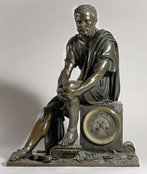 Neoclassical Style Bronze Figural Mantel Clock: Neoclassical Style Bronze Figural Mantel Clock Modeled in the form of a classically dressed bearded male with hands clasped around one knee, seated on a square piece of marble containing a clock face