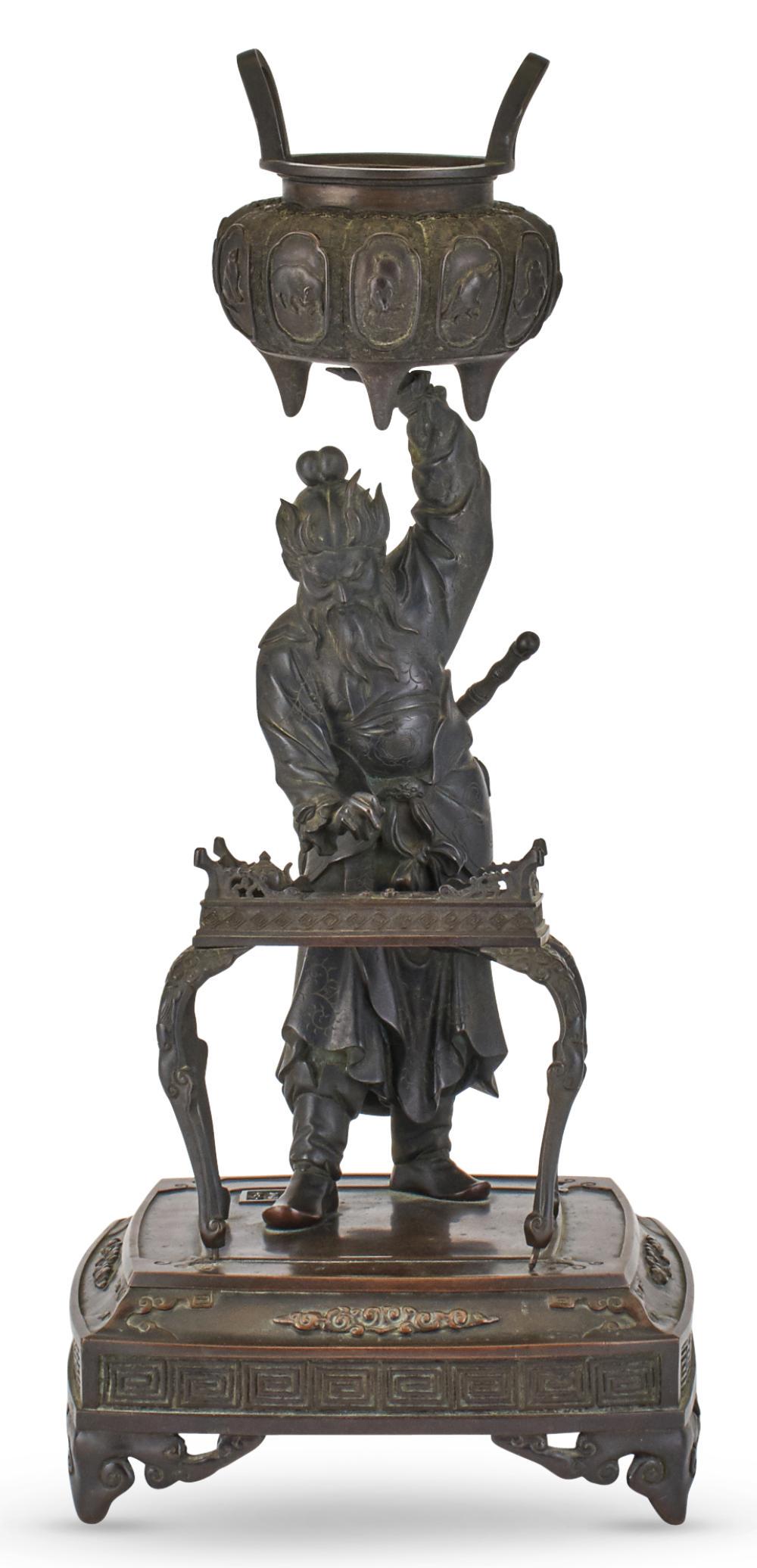 A Japanese Bronze Figural Okimono: A Japanese Bronze Figural Okimono Meiji Period Cast to depict the warrior Shoki holding up an enormous koro while casually standing at a writing table; mounted to platform base. Height 22 inches. C
