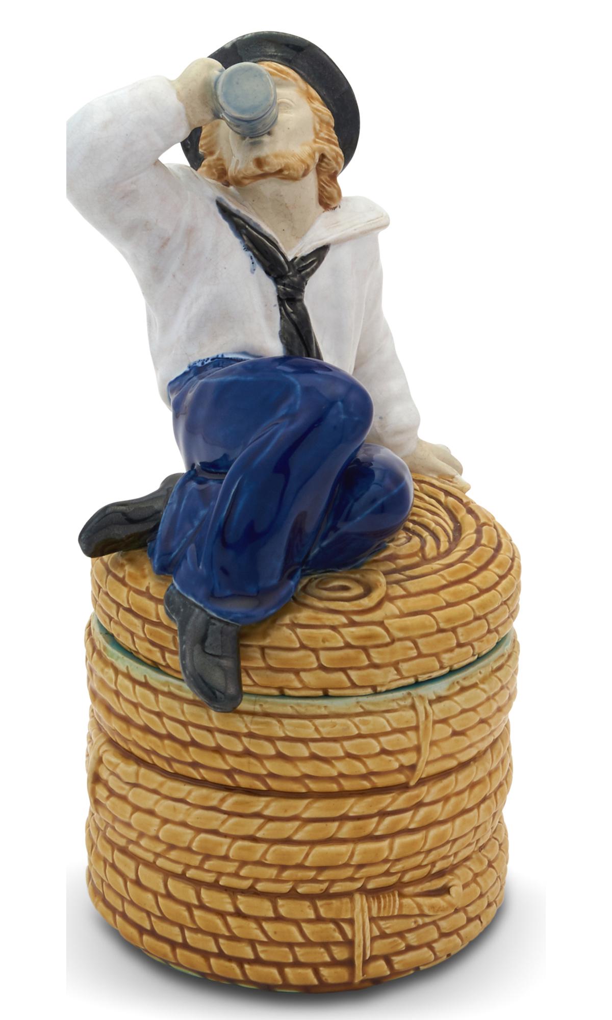 Minton Majolica Sailor Tobacco Jar and Cover Shape no. 716, date cypher possibly for 1872 Modeled as: Minton Majolica Sailor Tobacco Jar and Cover Shape no. 716, date cypher possibly for 1872 Modeled as a young, bearded sailor seated on a coiled rope spool, holding a pipe in his left hand and swigging
