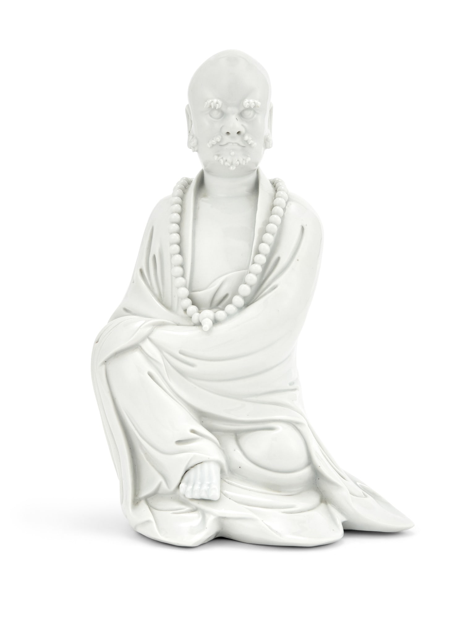 A Chinese Blanc de Chine Figure of a Seated Luohan 18th century: Depicting the seated and bearded figure in simple robes and wearing a strand of beads. Height 9 1/4 inches