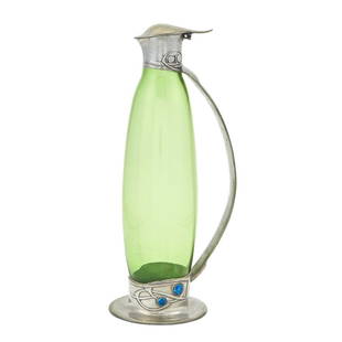 Archibald Knox for Liberty & Co. Pewter, Enamel and Glass Tudric Pattern Claret Jug: Estate / Collection: Property from a Gold Coast Long Island Private Collection The elongated oval body in transparent green colored glass, decorated with a mount with a Celtic-inspired stylized foliat