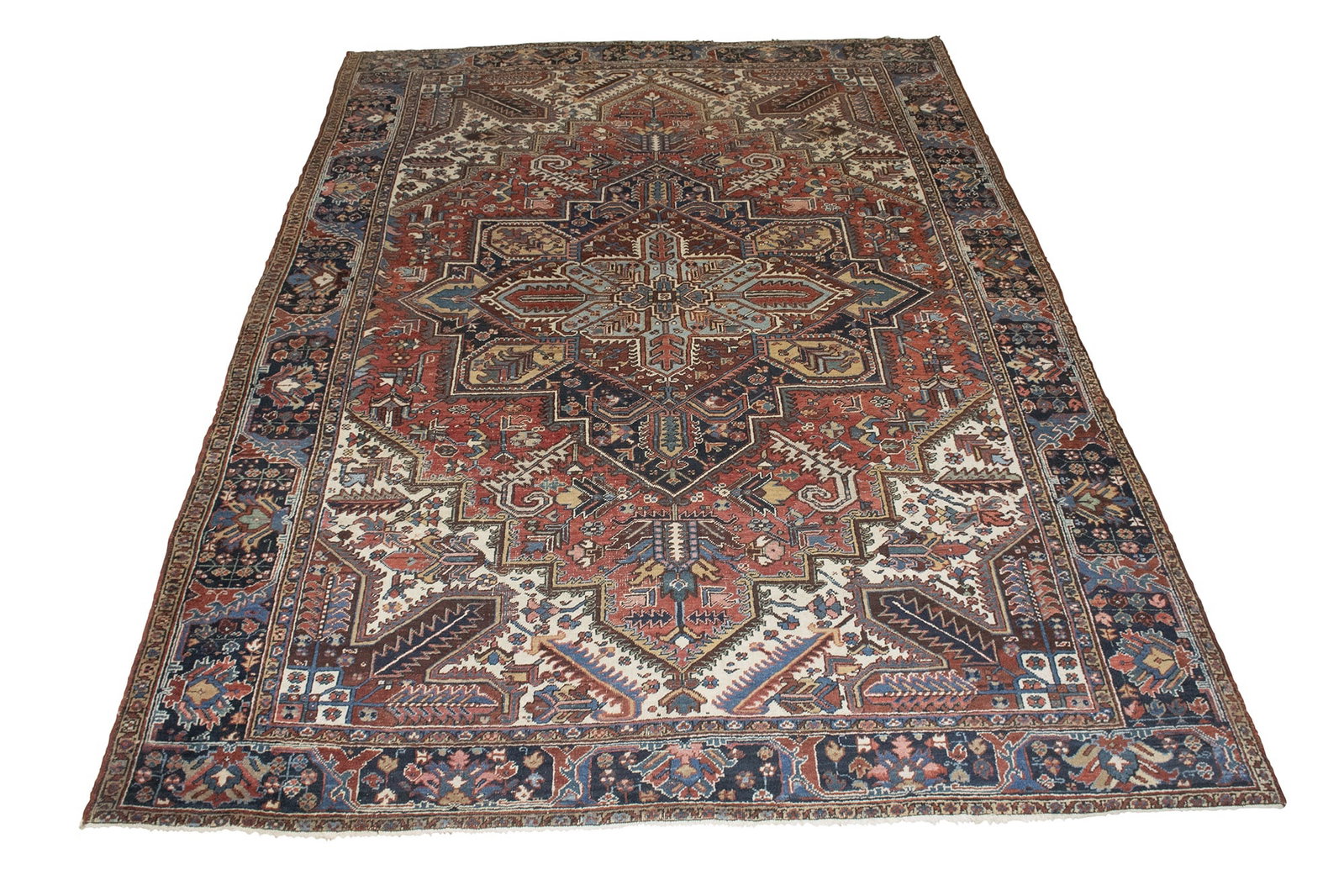 Heriz Carpet: Northwest Persia, Circa 1935 The central geometric medallion on the madder field flanked by ivory spandrels is within an indigo palmette and leafy vine border. (12' 2" x 9' 4")