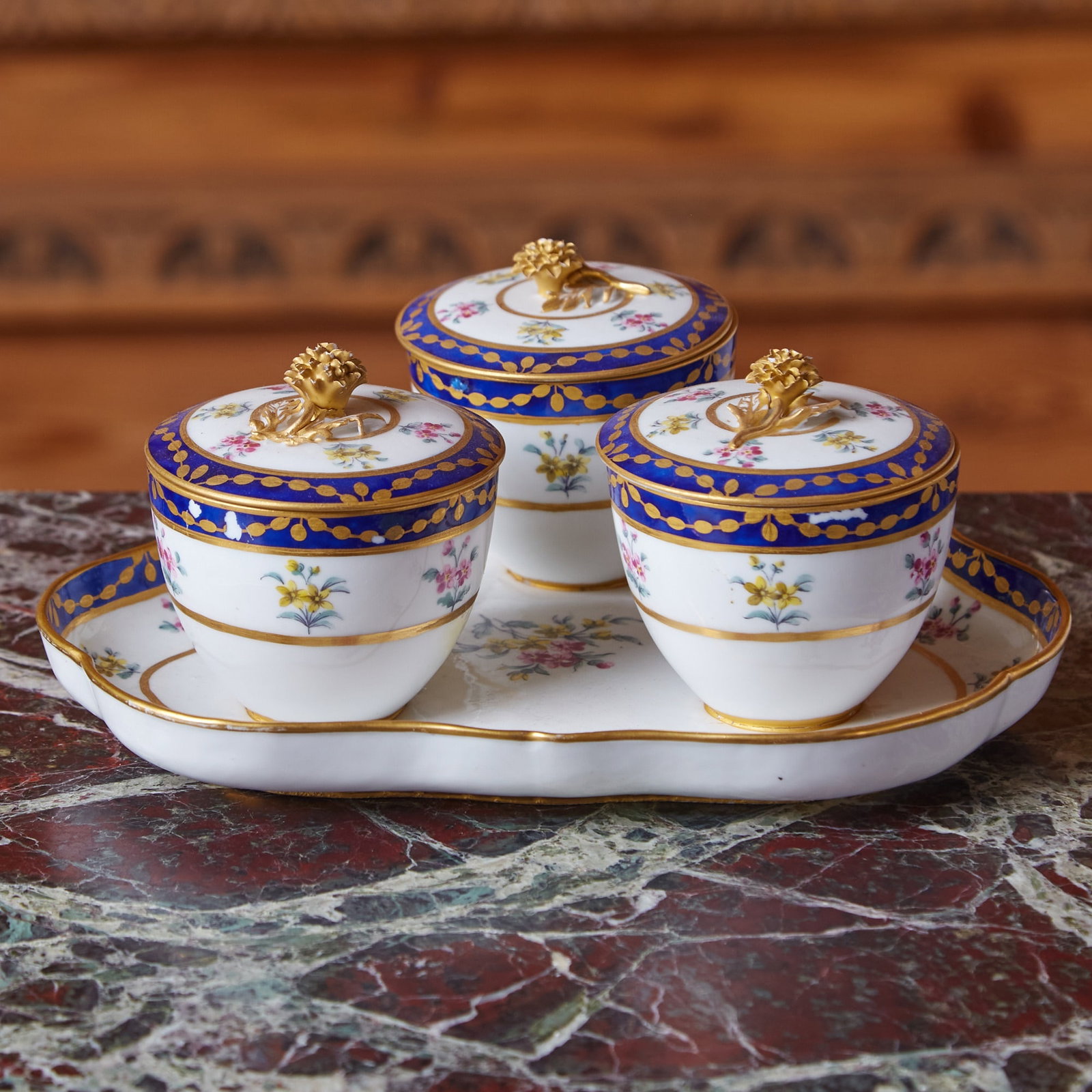 SAMSON PORCELAIN BLUE-BANDED TRIPLE JAM POTS AND COVERS FIXED ON A TREFOIL STAND Late 19th century: After the Sèvres form ‘plateau à trois pots de confiture', the covers with ranunculus finial, painted with small pink and yellow flower sprays, the blue banded borders enriched with gi