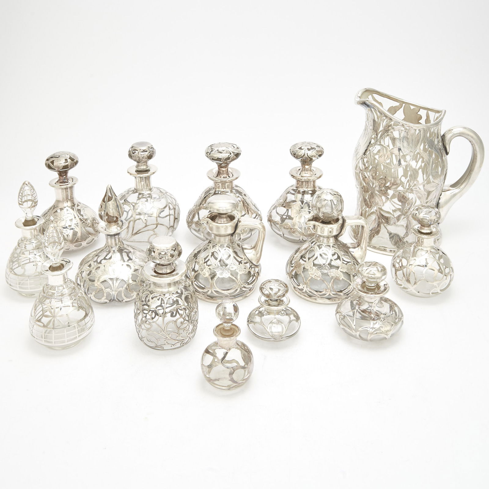 Group of Sterling Silver Overlaid Colorless Glass Table Articles Late 19th/ early 20th century: Including a water pitcher, height 8 1/4 inches; pair of cruet bottles, height 4 3/4 inches; scent flasks, etc. Approximately fourteen pieces.