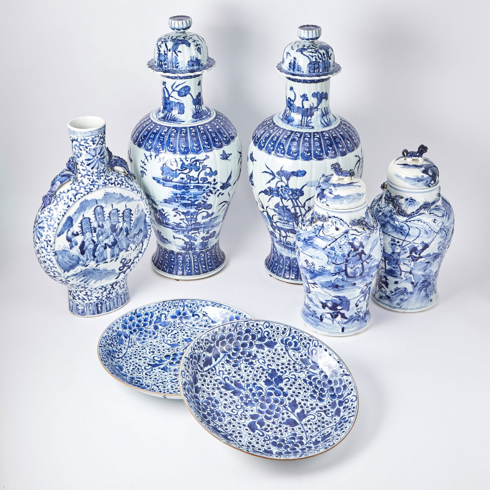 A Group of Chinese Blue and White Porcelain Vessels 19th/20th Century: Comprising a pair of baluster-form covered jars, a pair of baluster-form covered jars with fu dog finials, a pair of shallow chargers, and a moon flask vase. (Height of tallest 25 inches)