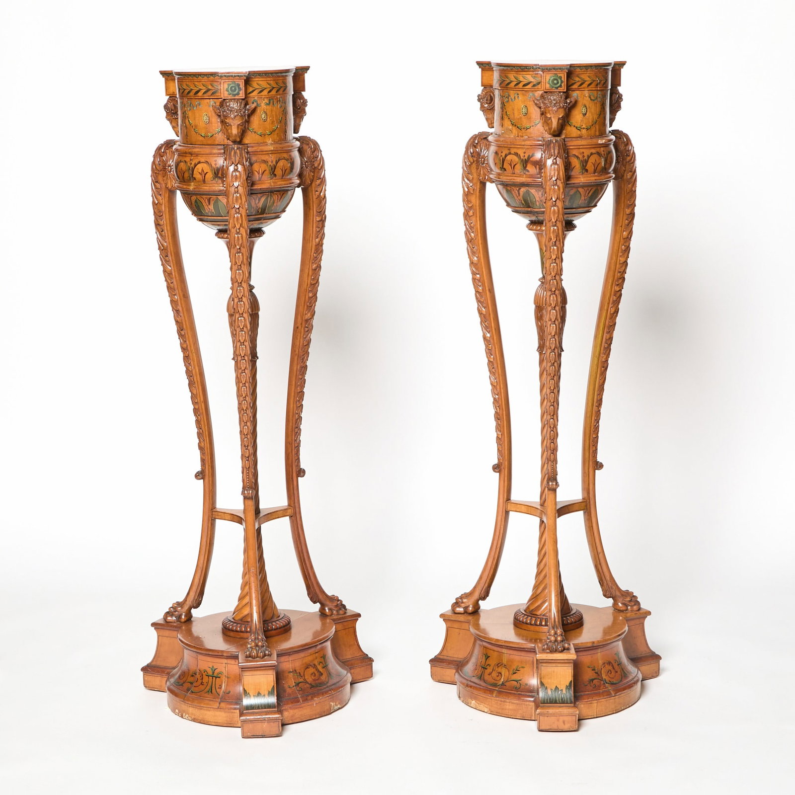 Pair of George III Style Painted and Carved Satinwood Torcheres Circa 1900: In the Adam style with painted garlands and rosettes. Finely carved Ram's Heads, columns and legs terminating in paw feet. One pedestal with a Made In England label underneath. Height 54 inches, Diame