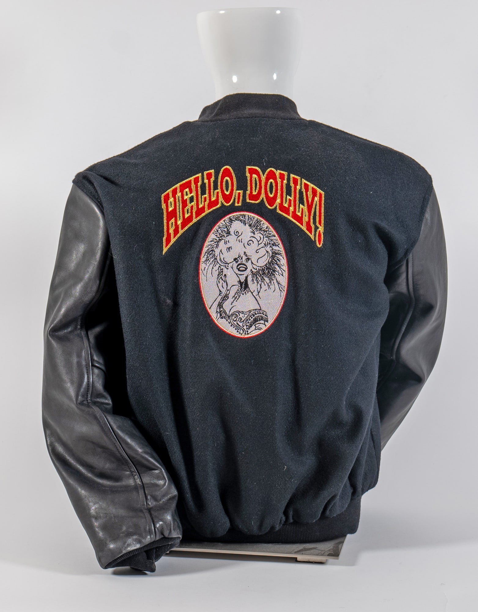 Hello Dolly Black Leather and Wool Bomber Jacket Sichel Personalized Promotional Sportswear Studio: With an embroidered logo on the back and an appliqued oval design of Carol Channing as Dolly. The front left breast is embroidered 'Jerry'. Quilted satin lining, zippered pockets.
