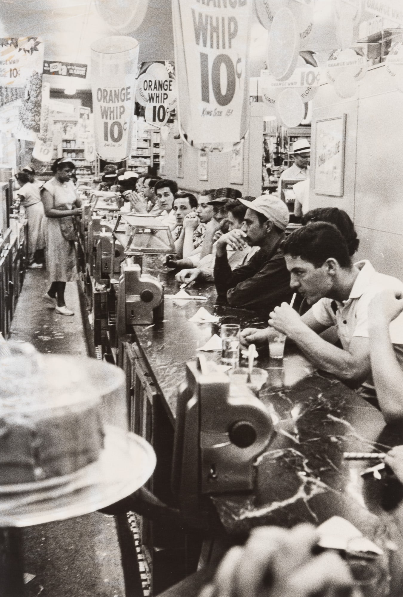 Robert Frank, Detroit (drugstore), 1955: FRANK, ROBERT (1924–2019) Detroit (drugstore), 1955, printed 1970s. Gelatin silver print 12 7/8 x 8 3/4 inches (327 x 222 mm) on larger sheet, with Frank's signature, title, and date (faded), in