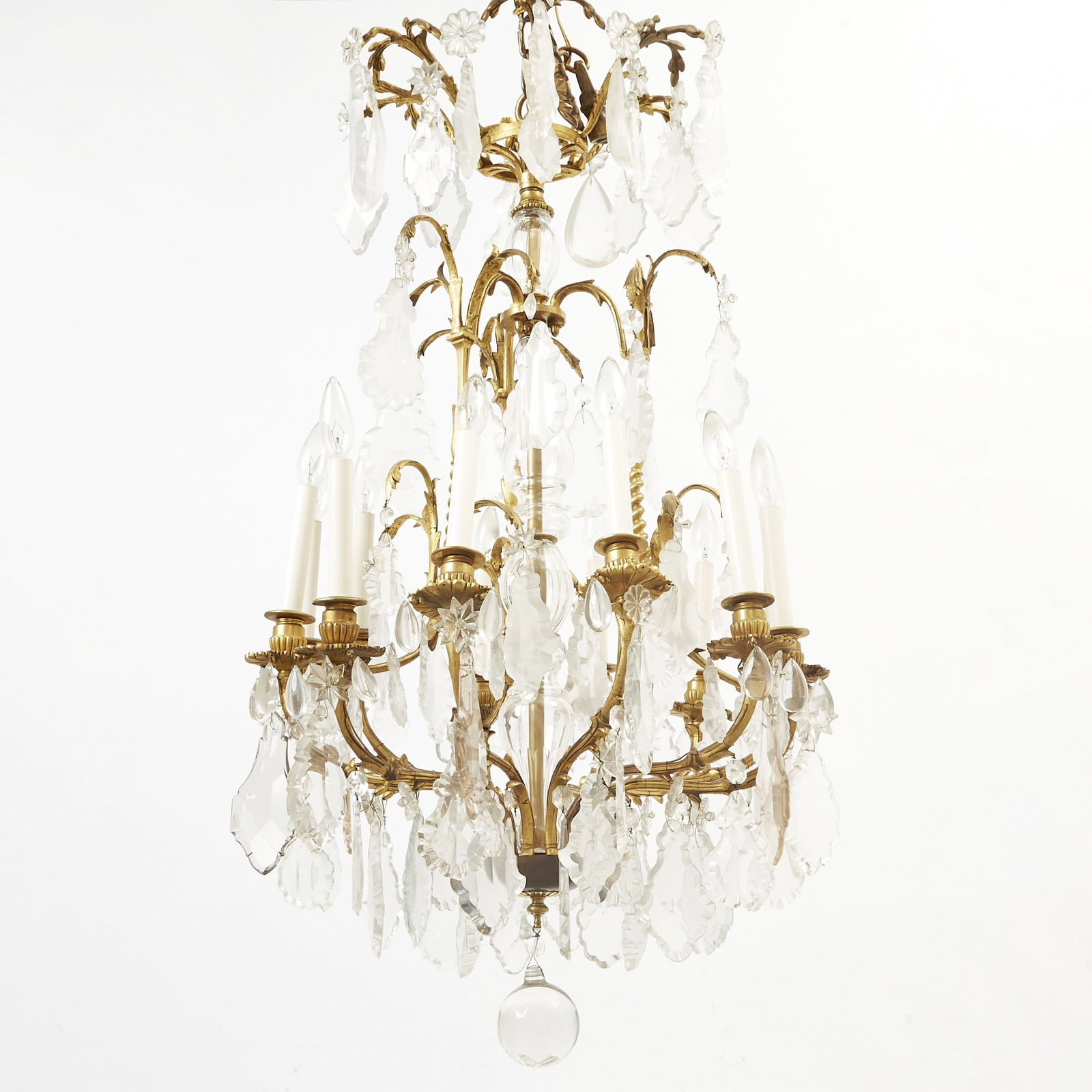 Louis XV Style Gilt-Bronze and Cut-Glass Twelve-Light Chandelier: The corona with shaped drops above a baluster stem issuing elaborately chased arms hung with rosettes, shaped drops and pendants above a pendent drop ball. Height 42 inches, diameter 23 inches.