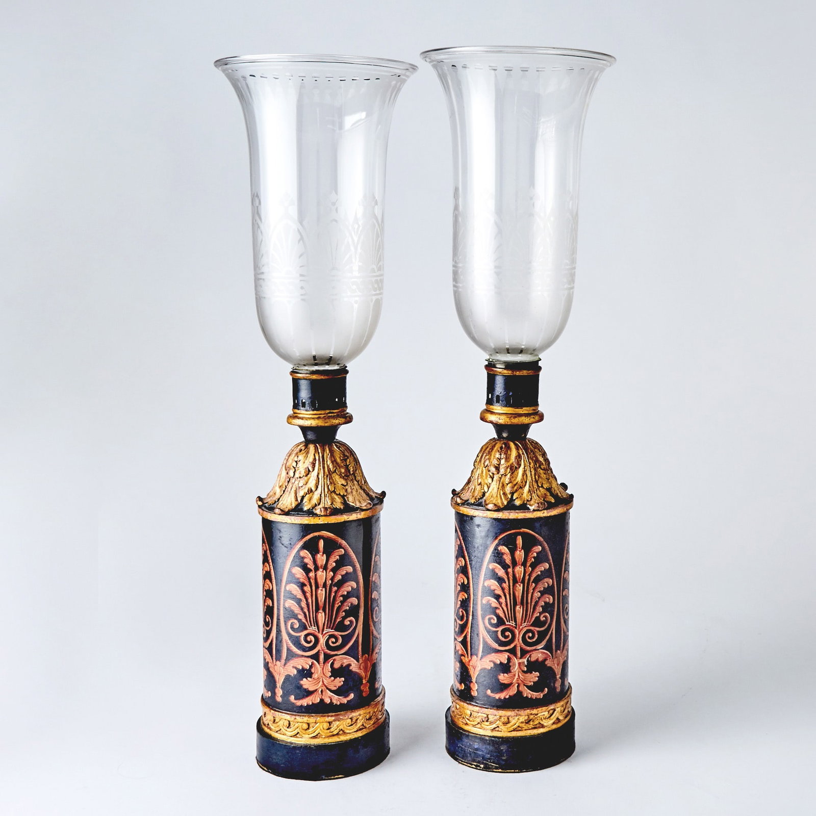 Pair Neoclassical Style Tôle Photophores: Each cylindrical circular base with transfer decoration of palmettes within above a vitruvian scroll border, surmounted by an inverted acanthus plume, with etched glass hurricane shades. Height overal