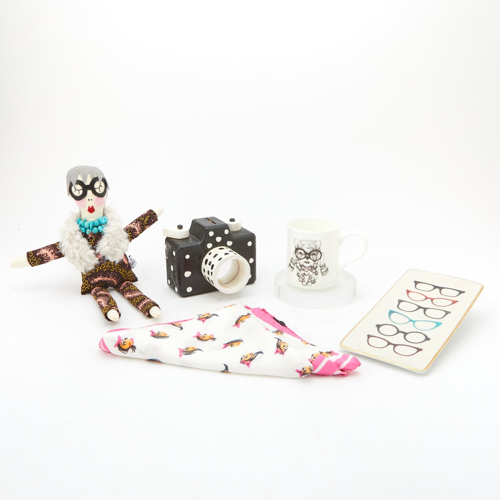 Group of Iris Apfel Ephemera: 20th/21st century Comprising black and white painted polka-dot wood camera model, a Rory Dobner fine bone china coffee cup, custom Iris Apfel stuffed doll, a Galison porcelain eye glass tray, and a cu