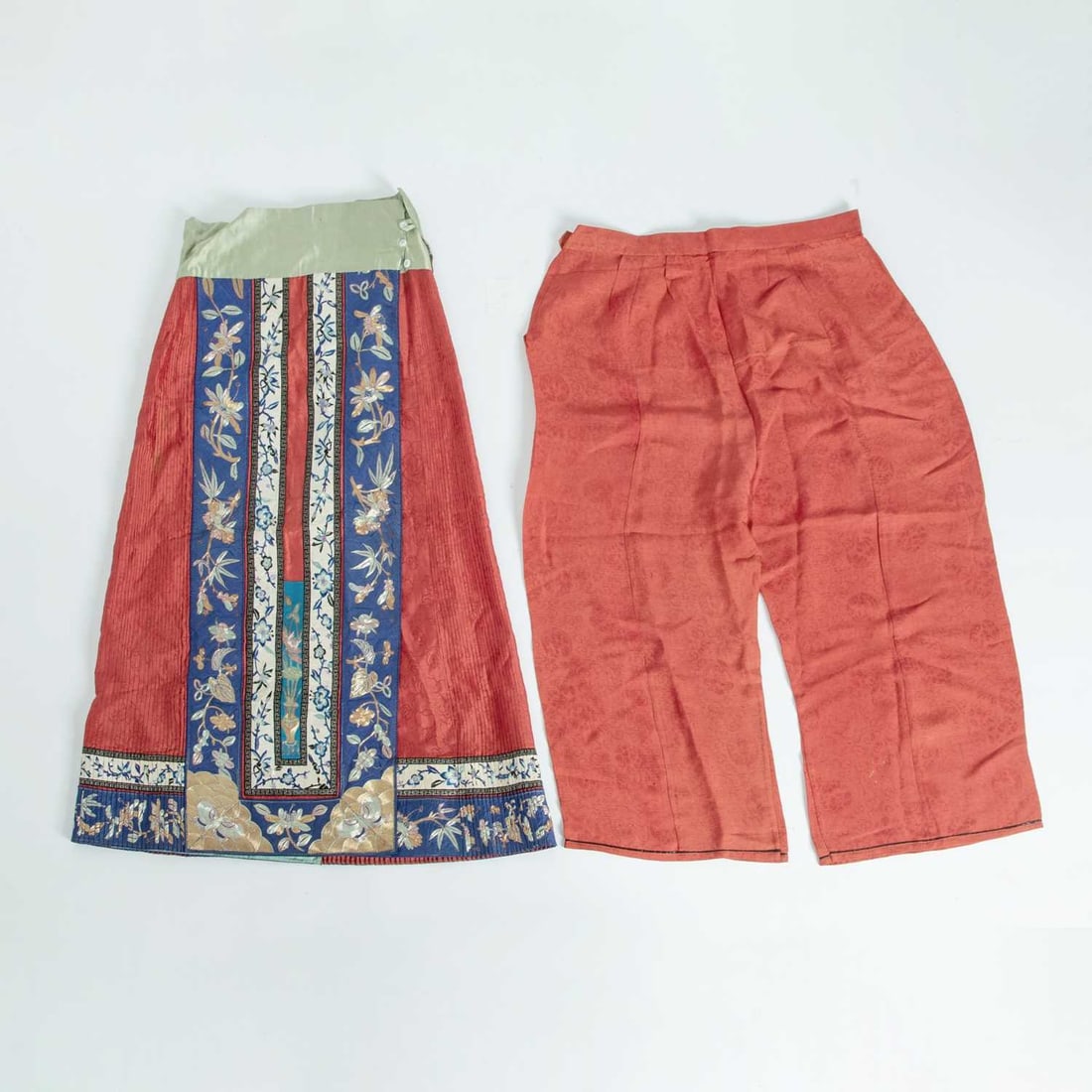 A Chinese Embroidered and Brocade Red Silk Skirt Late 19th Century: The pleated skirt is decorated with woven floral motifs on a red ground, with borders embroidered with flowering branches, blossoms, butterflies, and a vase; together with a pair of matching woven tro