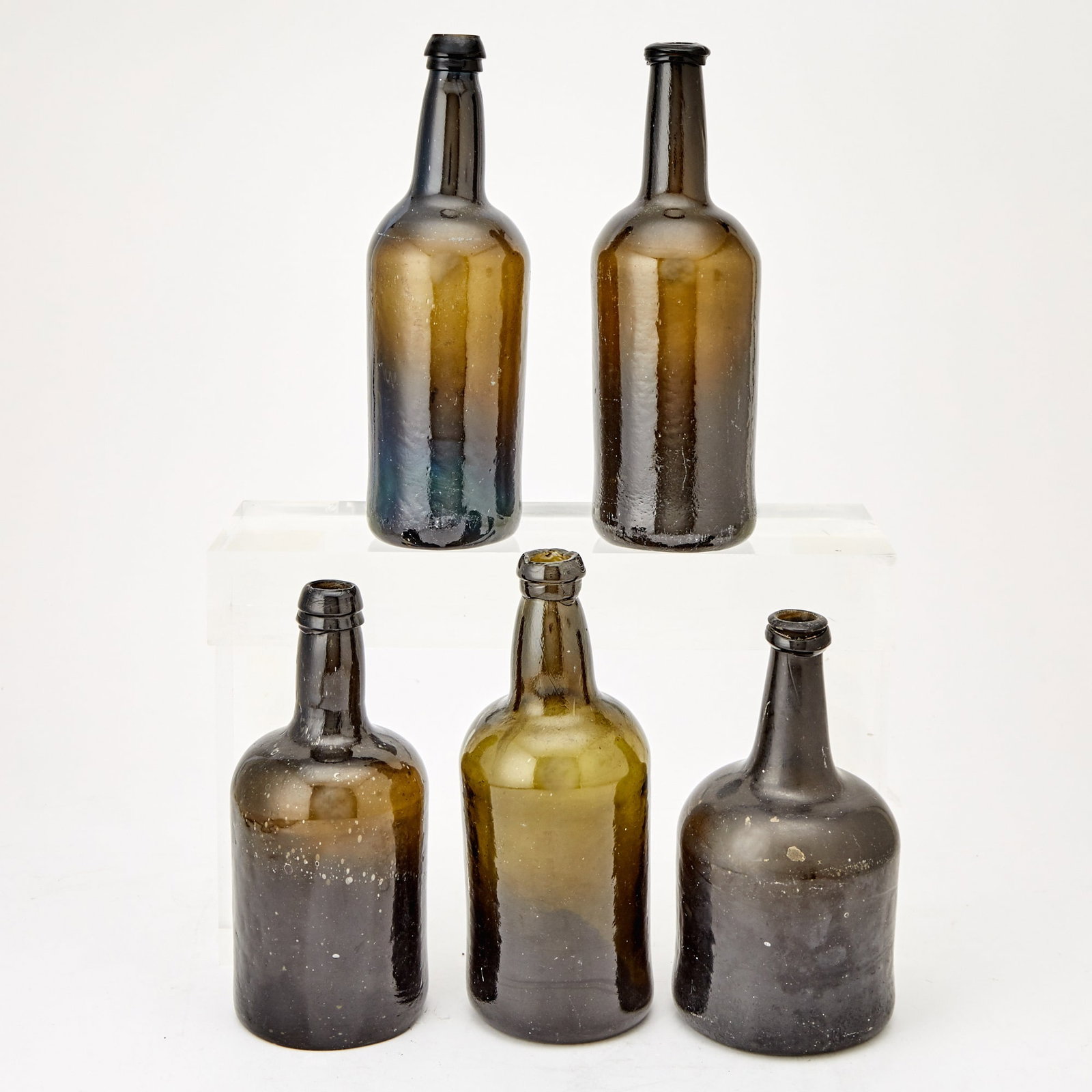 Group of Five Blown Olive Green Glass Wine Bottles: England or America, late 18th and early 19th century Each with concave punt. Height of largest 10 1/2 inches. varying degrees of scratching and wear.
