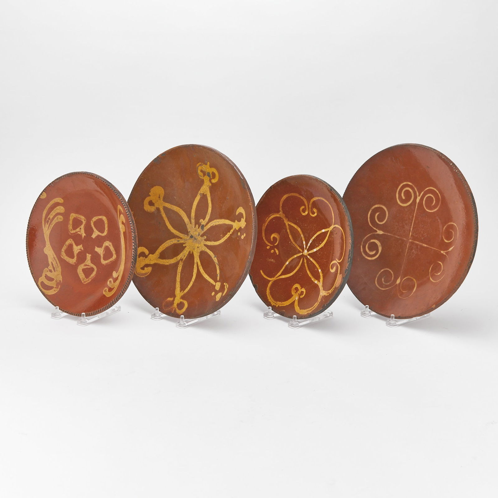 Four Glazed Redware Slip-decorated Plates 19th Century: Probably Huntington, Long Island, New York, 19th century Each with coggled rim and varied yellow slip decoration including squiggles, curlicues, and stylized flowers. Diameter of largest 11 1/4 inches