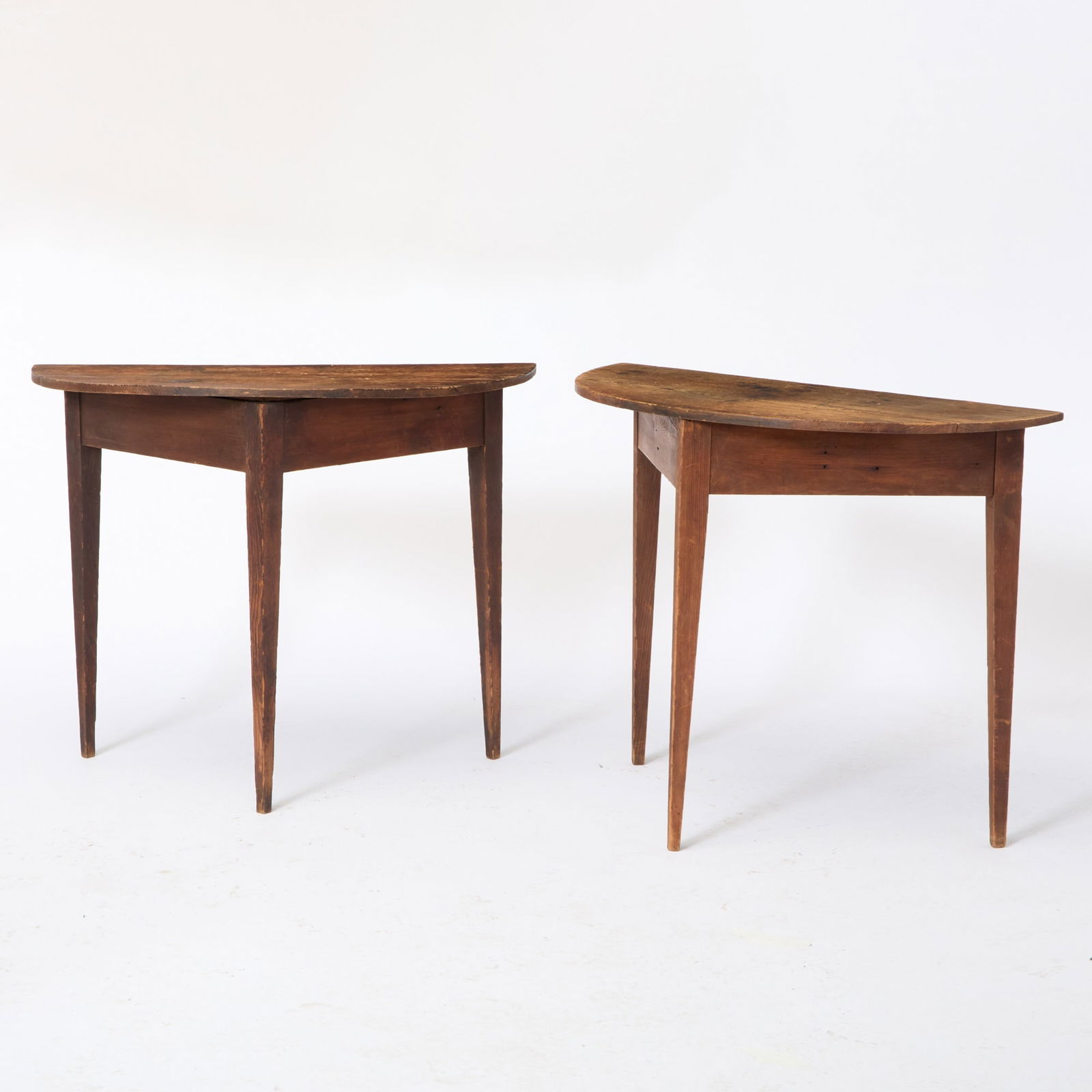 Near Pair of Red-Painted Pine Demilune Console Tables: New England, early 19th century Each with a straight apron, raised on three square tapering legs. Height 30 inches, width of larger 37 1/2 inches, depth of larger 18 inches.