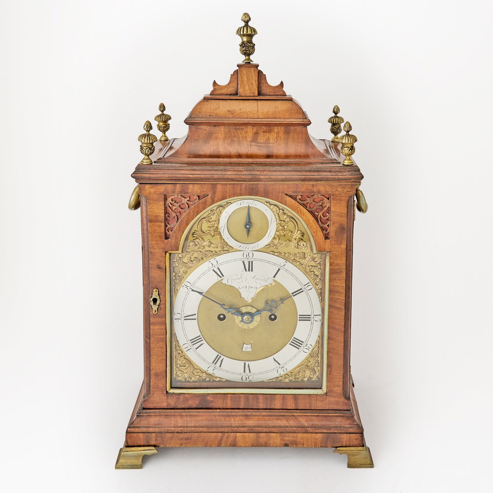 George III Brass Mounted Walnut Bracket Clock: Circa 1770, William Creak and James Smith, London The arched mahogany pediment with acorn brass finials above a glaze door enclosing a silvered metal chapter ring with Roman and Arabic numerals and in