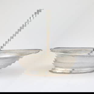 George III Sterling Silver Cake Basket: John Lamb, London, 1784 The oval body with beaded rim and pierced scroll, with pierced urns in medallions and engraved scrolling vine, with beaded overhead swing handle, on an oval foot. Height over h