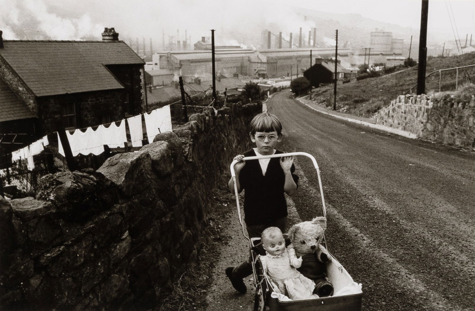 Bruce Davidson, Child in glasses pushing stroller with doll and teddy bear], 1965: DAVIDSON, BRUCE (b. 1933) [Child in glasses pushing stroller with doll and teddy bear], 1965, printed later. Gelatin silver print, 6 3/8 x 9 3/4 inches (163 x 250 mm) dry mounted to card, signed in pe