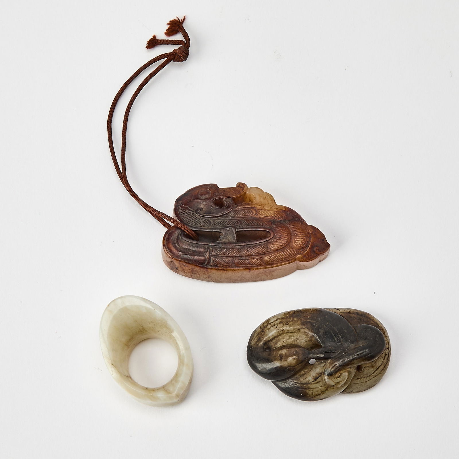 Three Chinese Jade Carvings Ming Dynasty: Comprising a 'mutton fat' jade archer's ring, a mottled jade carving of a goose, and a stylized russet jade carving of a duck. (Length of largest 2 1/2 inches)