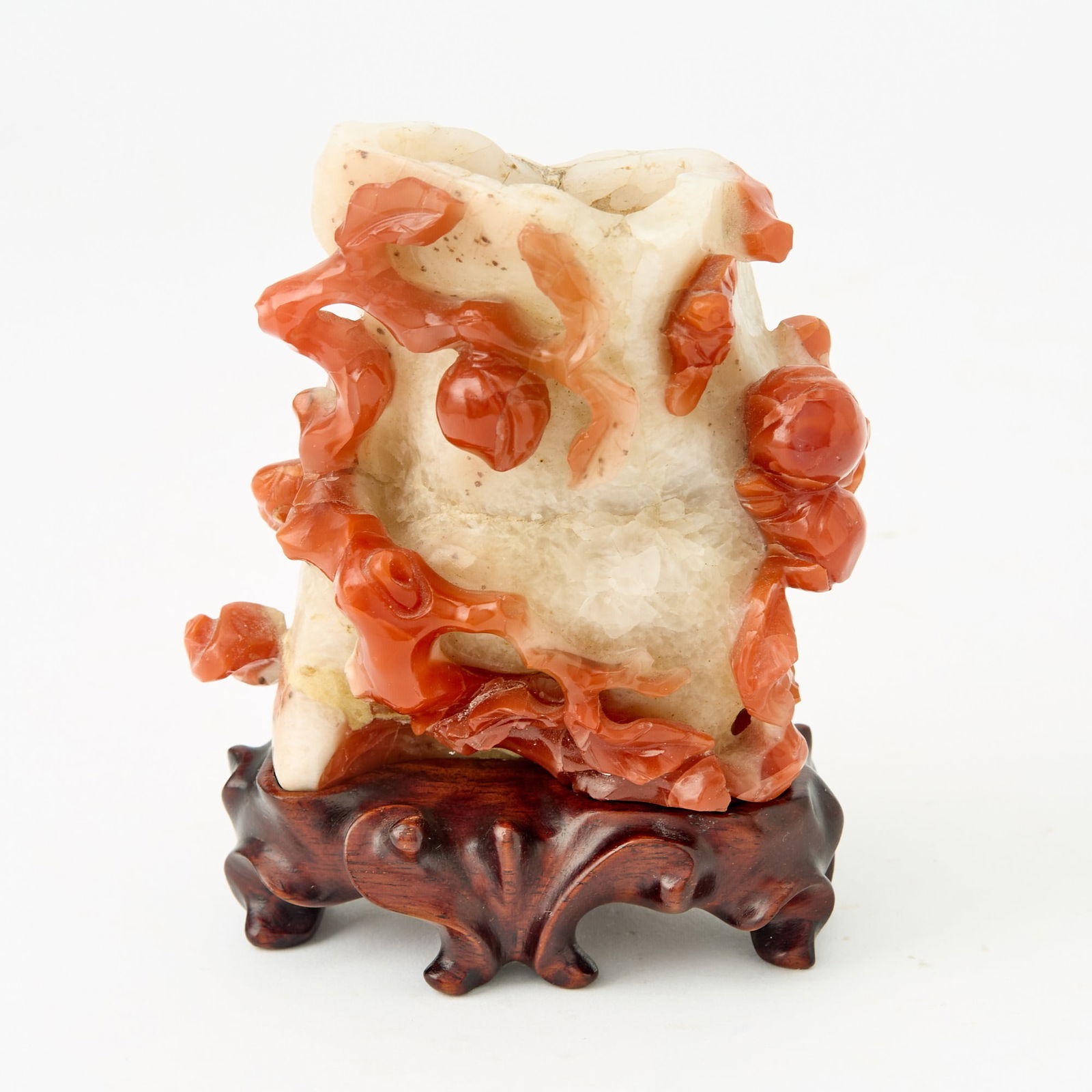 A Chinese Carved Carnelian Vase Late Qing Dynasty: Of naturalistic form; carved in relief to show peach boughs; with a wood stand. (Height 3 1/2 inches)