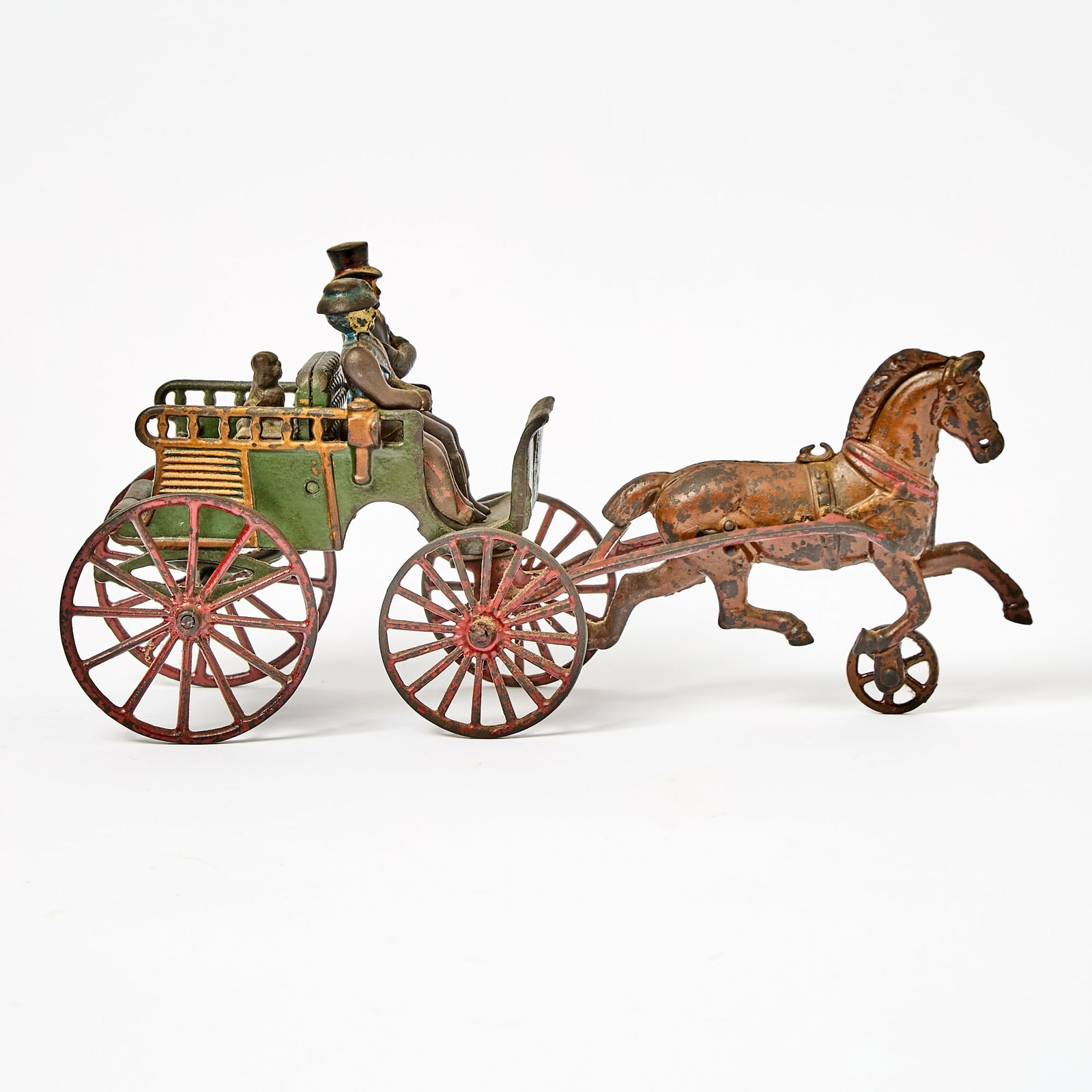 Painted Cast Iron Horse-drawn Buggy Toy: Circa 1900Green buggy with red wheels with two riders and a dog drawn by a brown hackney horse.Overall length 12 3/4 inches. Please note: This lot will be on view in Boston.
