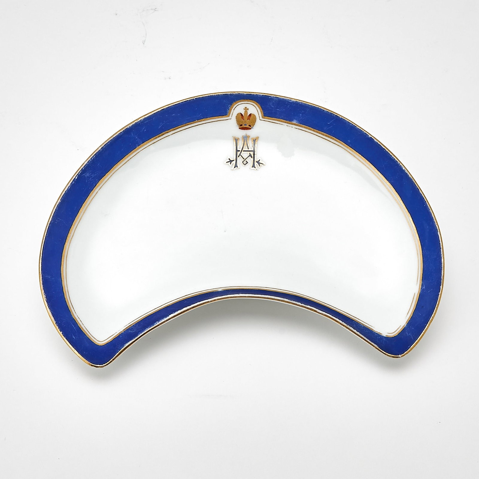 Russian Porcelain Plate From Tsarevich Nicholas Alexandrovich Service: Imperial Porcelain Manufactory, St. Petersburg, period of Nicholas II, dated 1898 Crescent shaped, with a blue and gilt line border, centering the gilt crowned cypher of Nicholas Alexandrovich. Width 