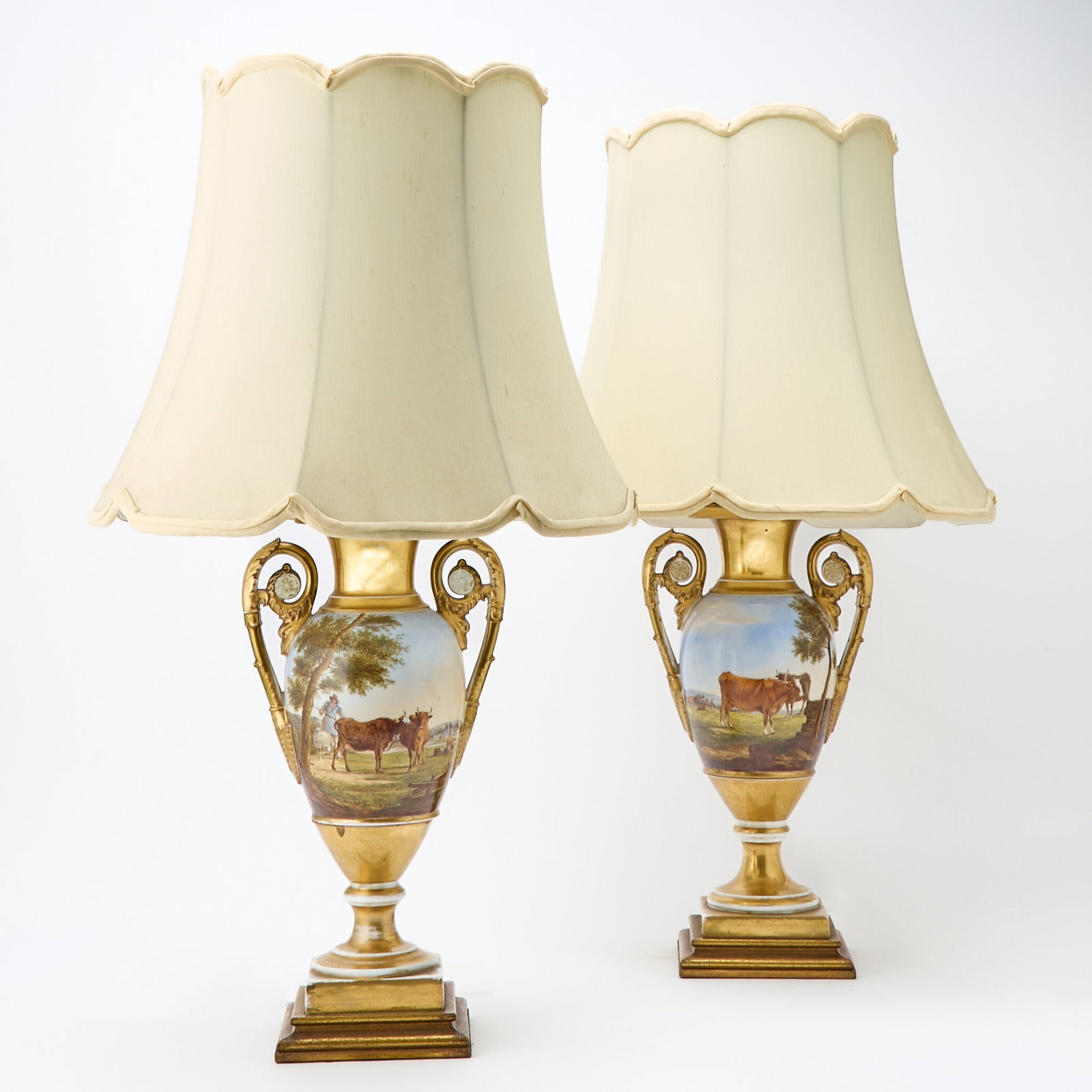 Pair of Paris Porcelain Gilt Ground Two-Handled Vases: First quarter 19th century Each baluster form with richly gilt ground, twin scrolling handles terminating in swan heads, on stepped square bases, and finely painted with pastoral landscapes, with cows