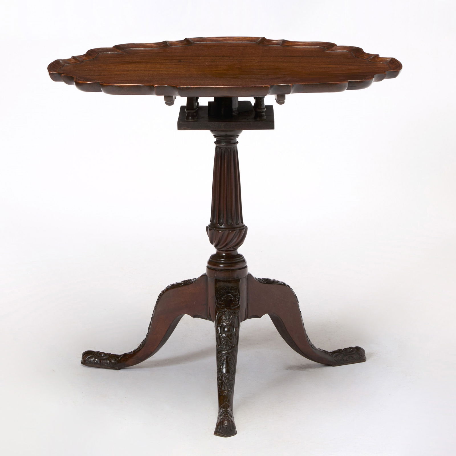 George III Style Mahogany Tripod Table: The top 18th century, the stem and legs 19th century The pie-crust circular top above a bird cage action and flaring fluted stem, the acanthus, cabochon, and C-scroll carved legs on pad feet. Height 2