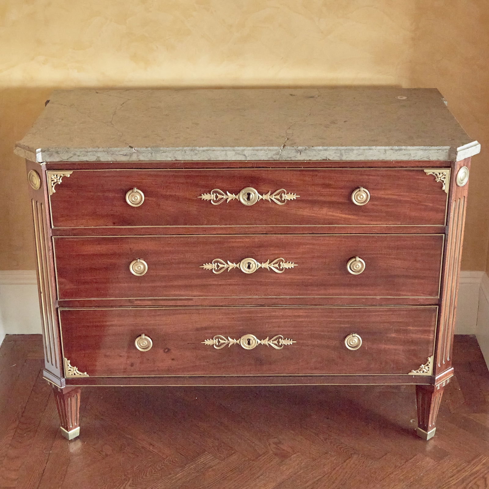 Swedish Neoclassical Gilt-Bronze Mounted Mahogany Commode: Circa 1785Of rectangular form, the molded grey marble top above three long drawers, the corners with ormolu foliate spandrels, raised on tapering legs. Height 33 3/4 inches, width 44 inches, depth 22