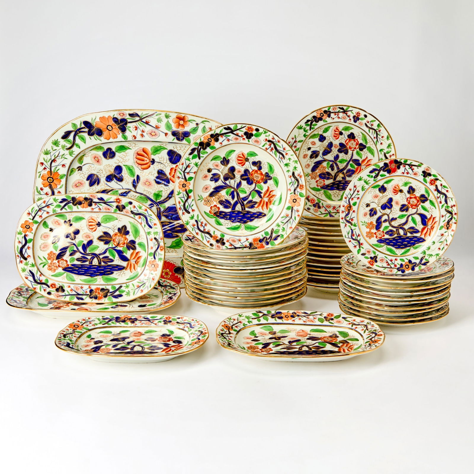 English Porcelain Partial Dinner Service: Early 19th century Each painted with stylized flowers in the Imari palette of underglaze blue and iron-red, enriched with bright enamels and gold gilt, comprising sixteen