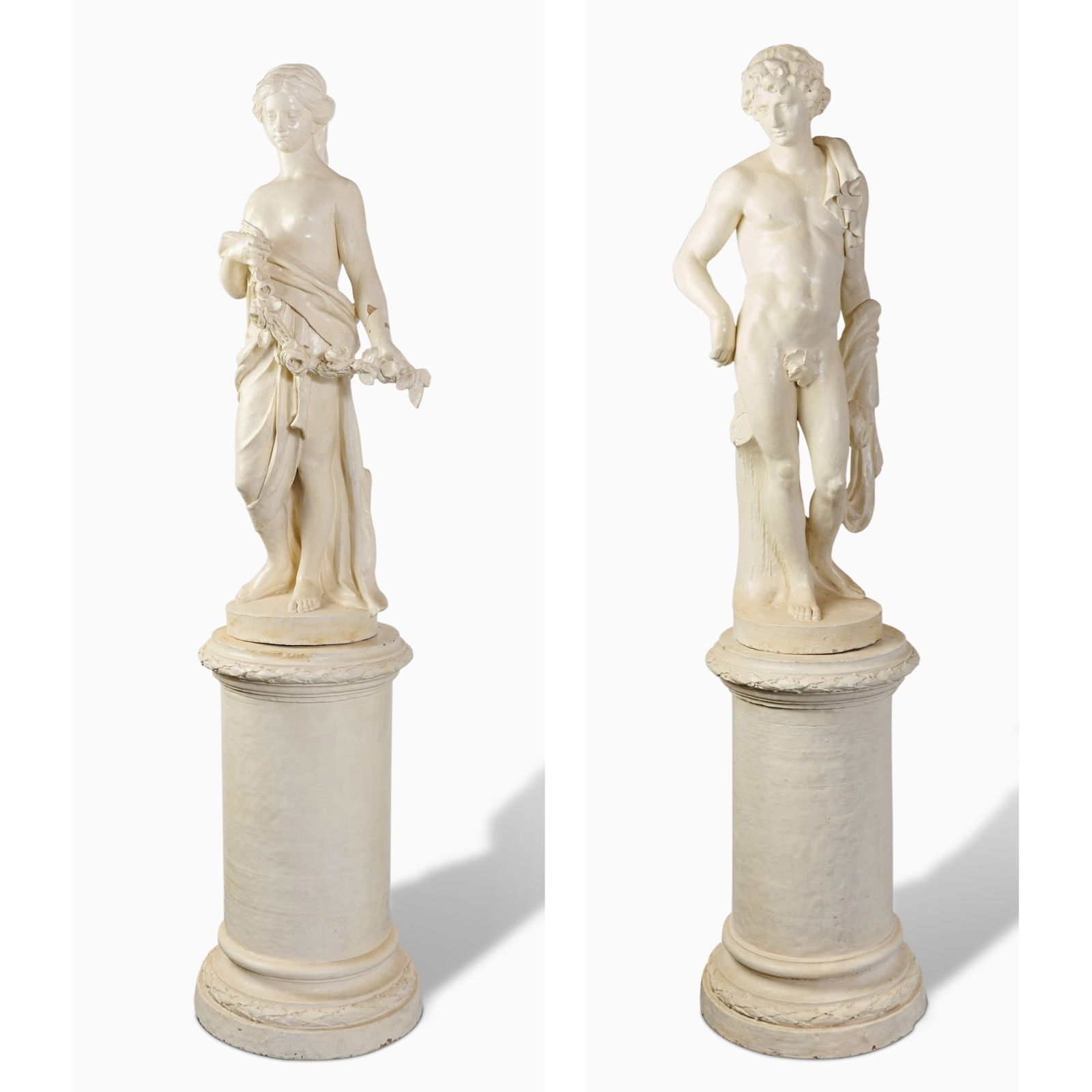 Pair of Italian White-Painted Terracotta Figures of a Maiden and a Youth on Pedestals: 19th century Each finely carved, the maiden draped in classical robes, holding a floral garland, the youth semi-nude with lion pelt over his shoulder, both on integral circular socle and cylindrical p