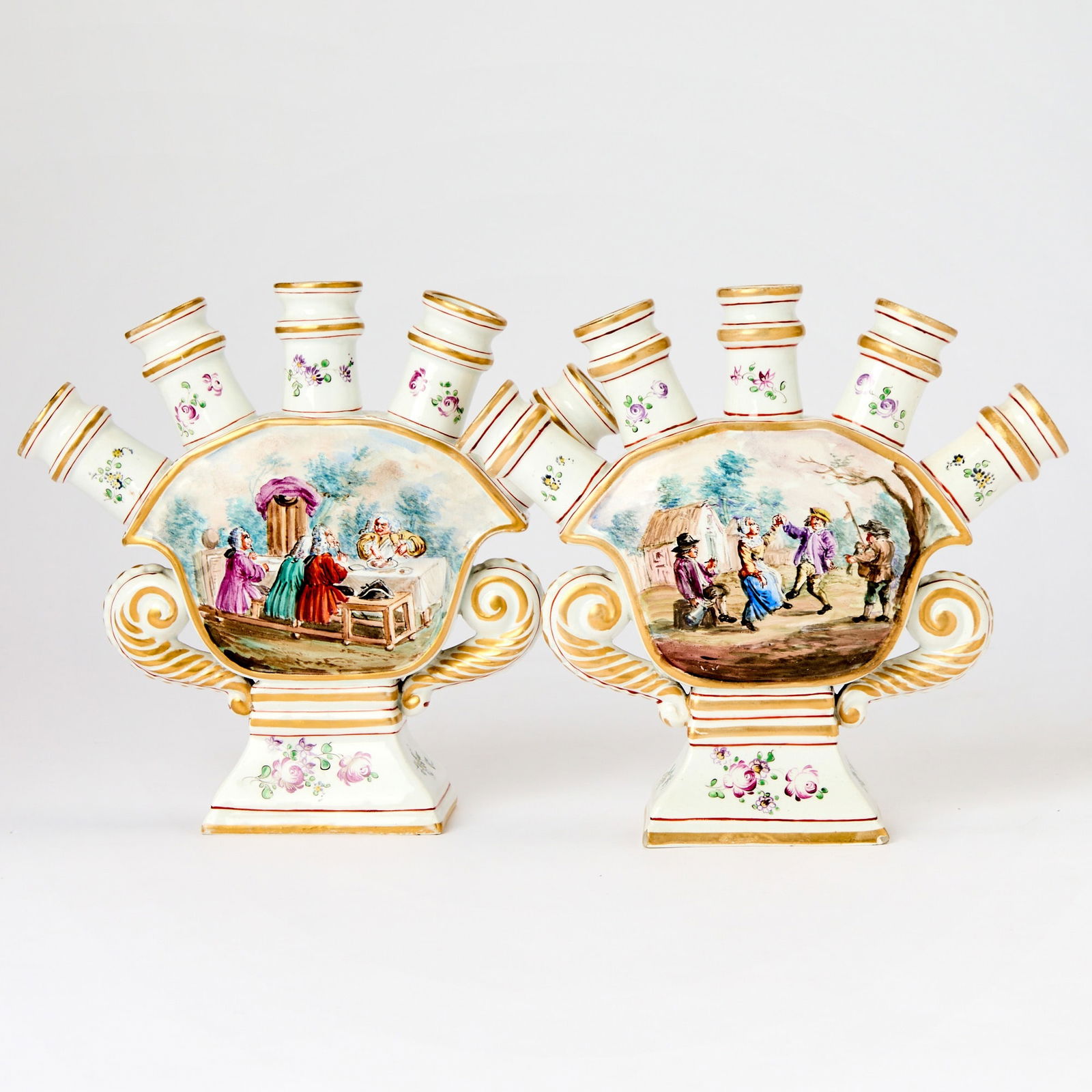 Pair of Hochst Damm Faience Tulipieres: Second half 19th century Each of flattened cartouche form, the center reserved with scenes of figures dancing and feasting, the reverse with floral sprigs, below four floral and gilt rimmed spouts, fl