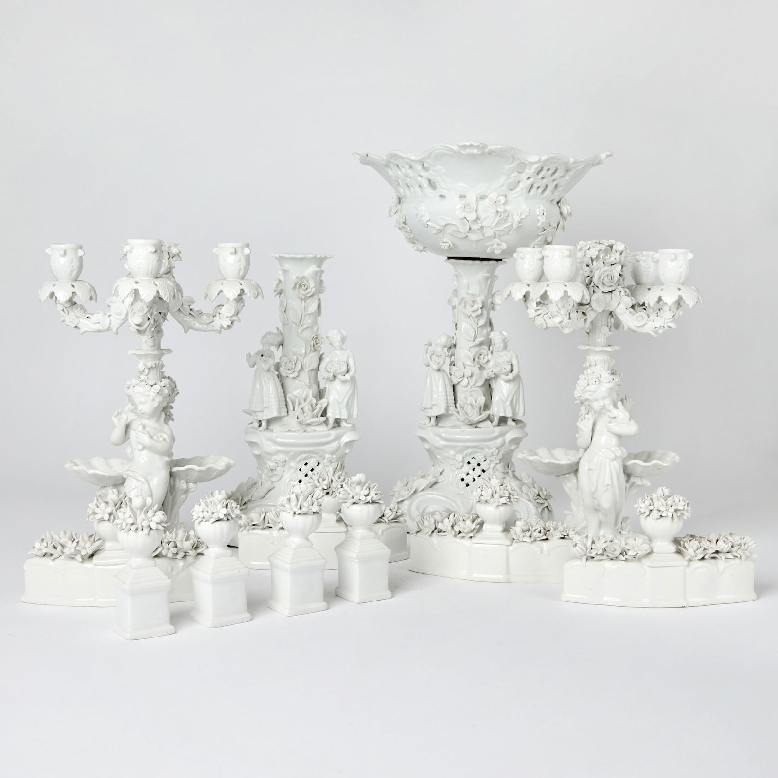 German Porcelain Surtout de Table: Circa 1880 Including a pair of Meissen porcelain four-light candelabra, each adjoining putto support with seashells and blossoms issuing four upscrolled floral candle arms with leafy bobeche and urn-f