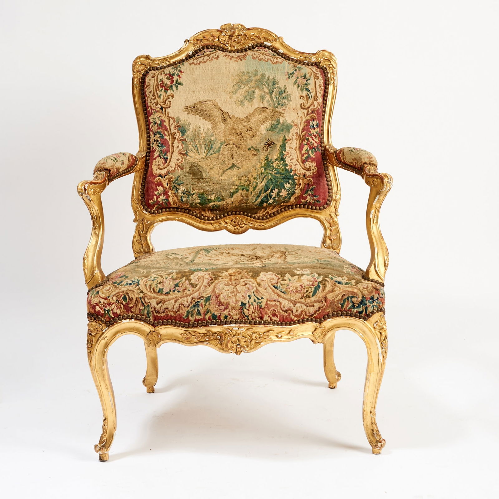 Louis XV Giltwood and Tapestry Fauteuil à la Reine: Mid-18th century The padded tapestry-upholstered back, arms, and seat, depicting a buzzard and lion within a leafy landscape, within a rocaille-molded and carved giltwood frame, on cabriole legs heade