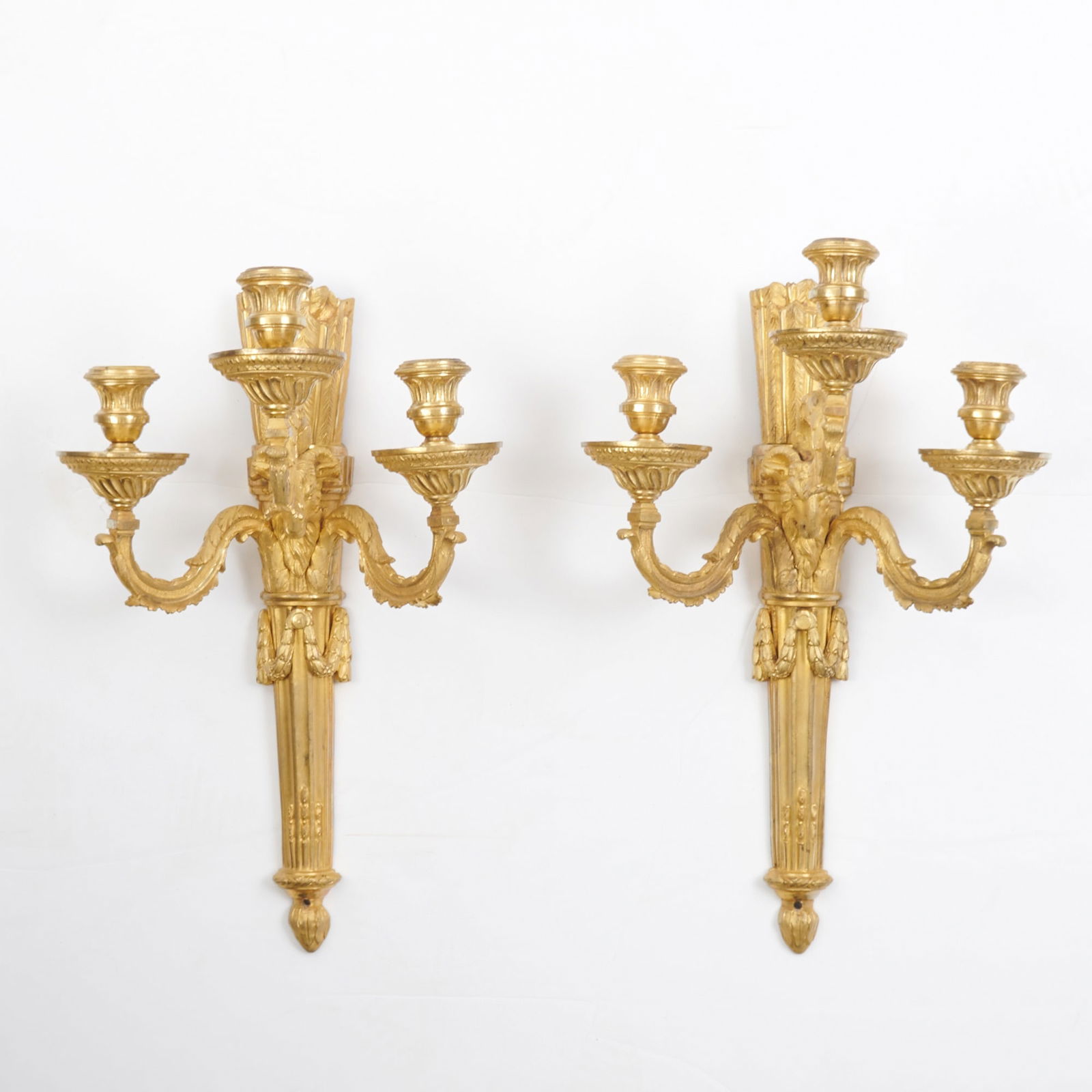 Pair of Louis XVI Ormolu Three-Branch Wall Lights: Circa 1780 Each with a stop-fluted shaft hung with floral garlands and in the shape of a quiver issuing three foliate scrolling branches with ram's head to base Height 18 inches (45.5 cm).
