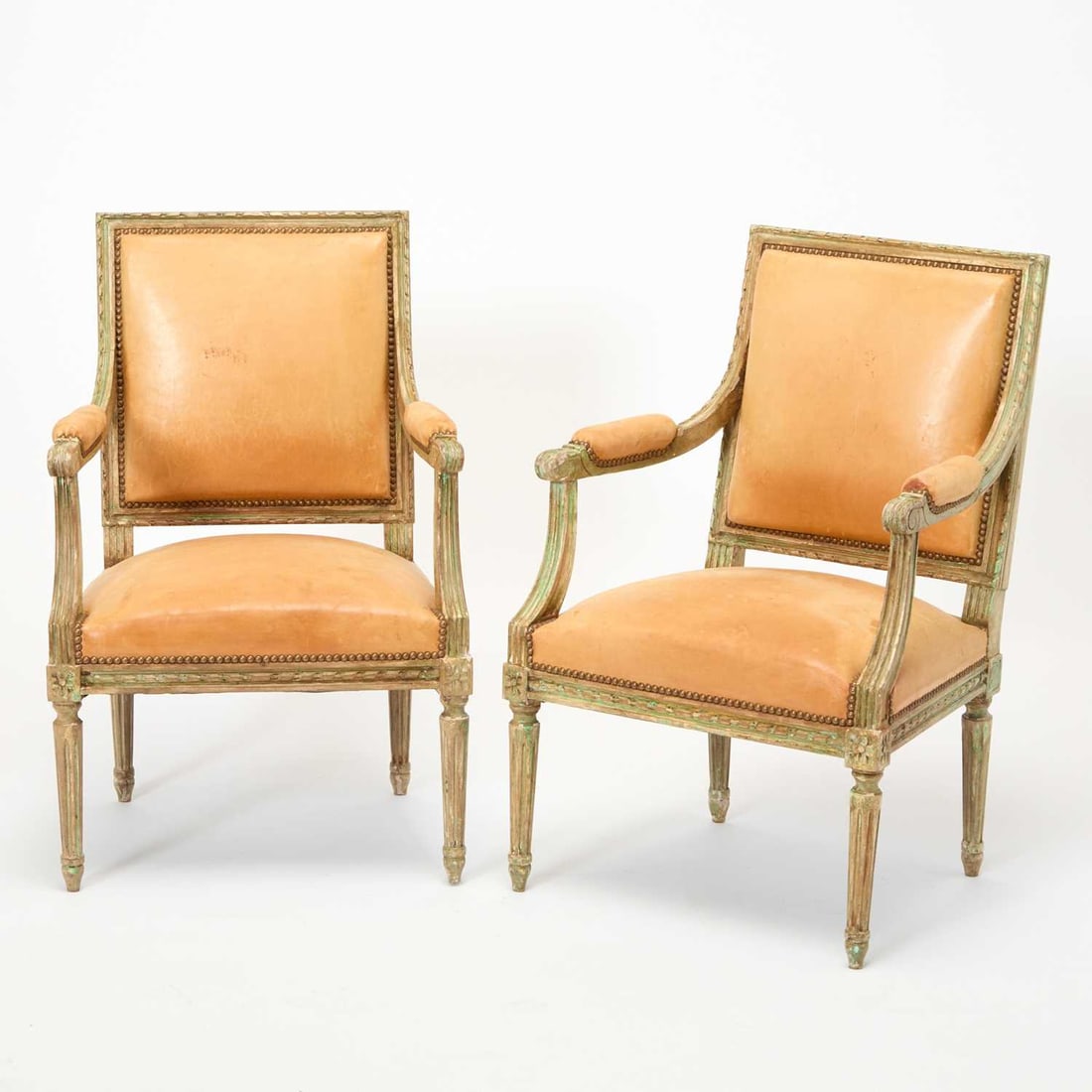 Pair of Louis XVI Leather Upholstered Painted Wood Fauteuils: Circa 1780 Heavily distressed finish painted in cream with light green highlights and a brown glaze. Height 35 inches, width 22 inches, depth 19 inches, seat height 16 inches. Provenance: Sotheby's.